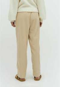 Beige, strukturiertes Hosen mit einer lockeren Passform, ausgestattet mit einem elastischen Bund und Seitentaschen, kombiniert mit braunen Sandalen.