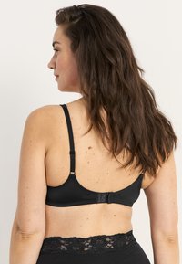 Svart bh med justerbara band, slät tyg och en hake-och-�öga stängning. Bandet har en spetsdetalj längs överkanten.