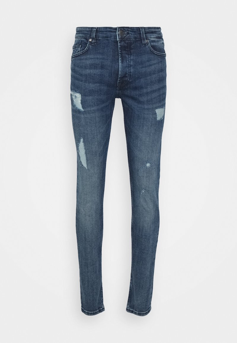 Jean slim bleu foncé avec des patches usés sur les cuisses et les genoux, fermeture à boutons sur le devant et design classique à cinq poches.