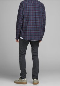 Kostkovaná košile v modré, červené a bílé barvě; tmavě šedé džíny; světle hnědé tenisky. Důraz na neformální, pohodlný střih a klasický design.