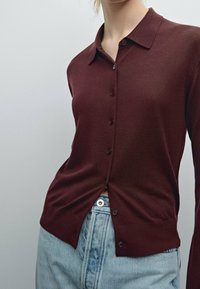 Bordeaux kleurige cardigan met een knoopsluiting aan de voorkant, klassieke kraag en geribde manchetten, gecombineerd met lichtblauwe denim jeans.