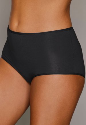 Frau, die schlichte schwarze Baumwollunterwäsche mit hoher Taille trägt, zugeschnitten, um den Oberkörper und die Oberschenkel zu zeigen, vor neutralem Hintergrund.