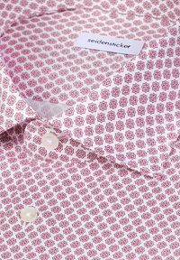 Chemise blanche avec un motif géométrique rouge et deux boutons blancs visibles, dotée d'un col et d'une étiquette "seidensticker".