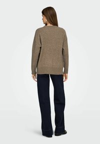 Brauner Strickpullover mit lockerer Passform, überschnittenen Schultern und geripptem Saum, kombiniert mit marineblauen weit geschnittenen Hosen. Glatte Textur, lässiges Design.