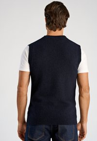 Marineblauer ärmelloser Strickpullover mit strukturierter Oberfläche und gerippten Säumen, über einem weißen T-Shirt getragen. Lässiges Design mit figurbetonter Passform.