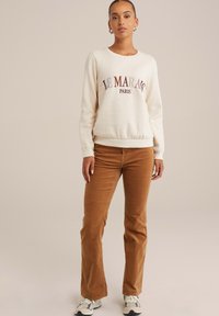 Beige pulóver "LE MARAIS PARIS" burgundi betűkkel, világosbarna kordbársony nadrággal és szürke tornacipővel párosítva. Sima felület, laza fazon.