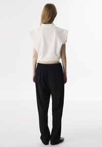 Pullover bianco tagliato con colletto alto espalle larghe abbinato a pantaloni neri larghi con cintura elastica.