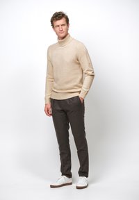 Beige polokrage tröja i mjukt stickat material, kombinerad med mörkgrå skräddarsydda byxor och vita sneakers. Enkelt design, figursydd siluett och rena linjer.