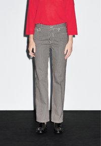 Pantaloni a righe bianche e nere con vestibilità dritta, caratterizzati da un bottone e passanti per la cintura, abbinati a una maglietta rossa a maniche lunghe.