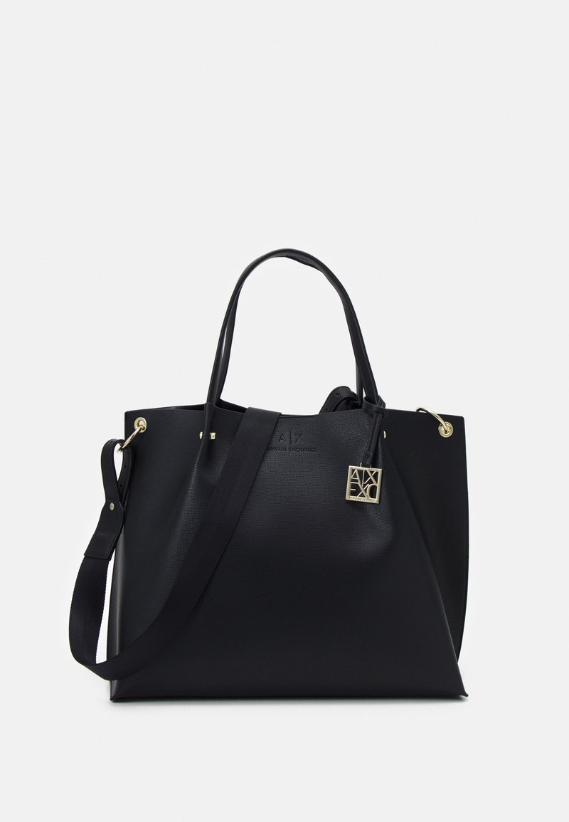 Sac fourre-tout en cuir noir avec deux poignées supérieures et une bandoulière amovible. Comprend des accessoires en métal doré et un charme logo. Texture lisse, design minimaliste.