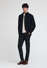 Czarna koszula kurtka z korduroy z dwiema kieszeniami na piersi, noszona na kremowym swetrze; zestawiona z czarnymi spodniami i ciemnoskórzanymi sznurowanymi butami.