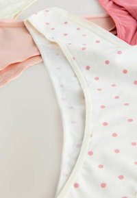 Drie paar vrouwen katoen ondergoed in roze, koraal en wit met roze stippen, overlappend op een vlakke ondergrond gelegd.