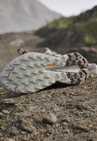 Podeszwa buta trekkingowego z głębokim bieżnikiem i logo Continental spoczywająca na skalistej, piaszczystej ścieżce w górskim terenie na zewnątrz.