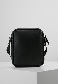 Černá kožená crossbody taška s texturovaným povrchem, obdélníkovým tvarem, zipovým uzávěrem a nastavitelným popruhem. Obsahuje stříbrné kování.