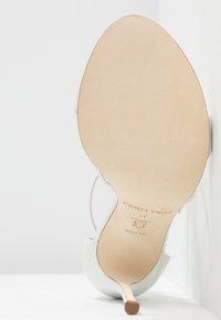 Chaussure à talon haut blanche avec un bout pointu, dessus en cuir lisse et semelle en cuir beige. Talon fin et design minimaliste.