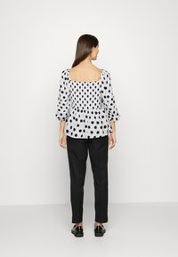 Blusa preta com bolinhas brancas, mangas bufantes, decote quadrado e costas com pregas, combinada com calças pretas e sapatos brilhantes.