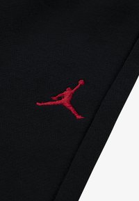 Crni materijal s izvezenim crvenim Jumpman logom, smještenim s lijeve strane, s glatkom teksturom i urednim završetkom.