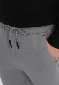Graue Jogginghosen aus weichem Material, mit einem elastischen Bund und Kordelzug, seitlichen Taschen und minimalistischen schwarzen Akzenten.