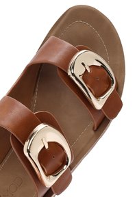 Sandales en simili cuir marron avec deux larges sangles et boucles dorées. Finition avec une semelle intérieure beige lisse et des détails de surpiqûres subtils.