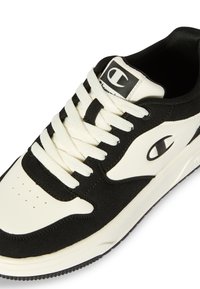Schwarzer und weißer Sportschuh mit einem Obermaterial aus glattem Leder und strukturiertem Wildleder, dicken Schnürsenkeln und einer Gummisohle mit einem gemusterten Profil.