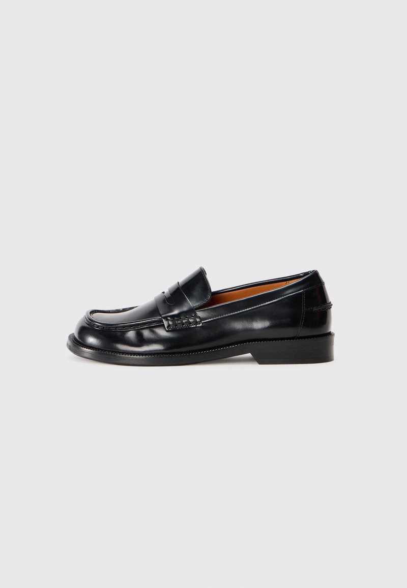 Svart, polert skinn penny loafer-sko med søm detaljer og lav hæl på en nøytral bakgrunn.