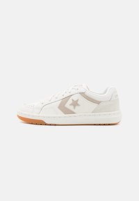 Baskets Converse basse blanches avec logo étoile beige et chevron, semelle en caoutchouc, et fermeture à lacets, présentées sur un fond uni.