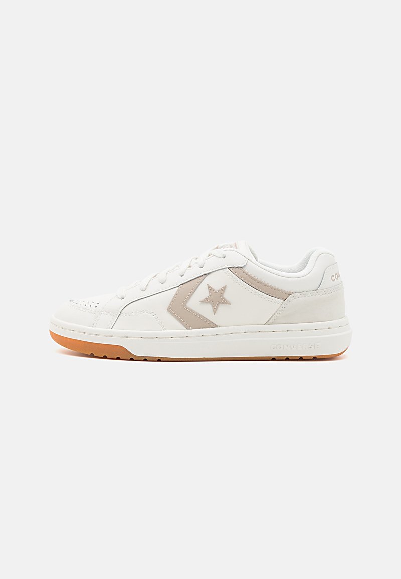 Baskets Converse basse blanches avec logo étoile beige et chevron, semelle en caoutchouc, et fermeture à lacets, présentées sur un fond uni.