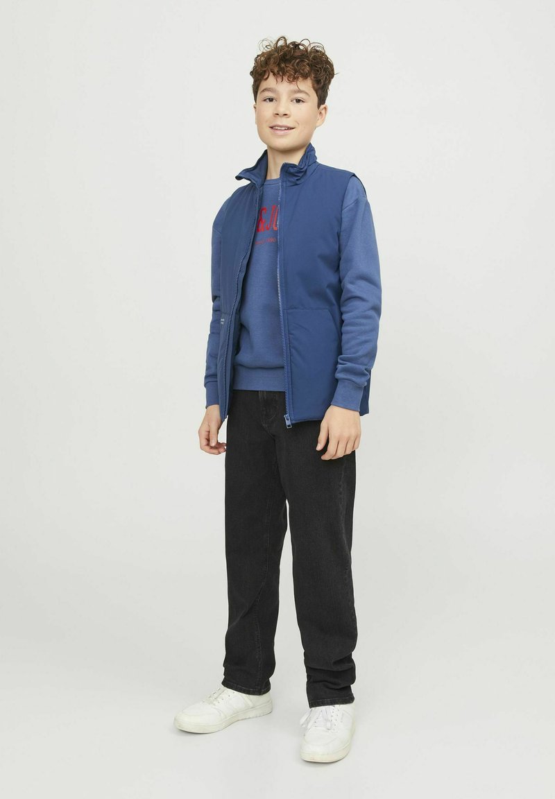 Marinblå zip-up jacka över en blå sweatshirt, kombinerad med svarta jeans och vita sneakers, som visar en avslappnad, lagerpåsatt outfitdesign.