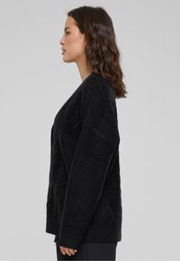 Zwarte gebreide cardigan met een gestructureerd ruitpatroon, lange mouwen en geribde manchetten en zoom, met een relaxte pasvorm en zacht materiaal.
