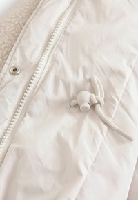 Witte jas met een gewatteerde fleece voering, zijrits en een trekkoord met een plastic togglesluiting. Soepele stof met een matte afwerking.