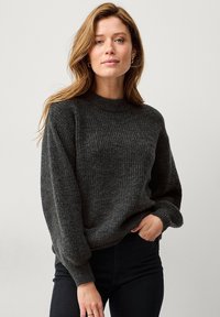 Donkergrijze gebreide trui met een geribbelde structuur, ronde halslijn en lichtgepofte lange mouwen. Combinatie met zwarte broek.
