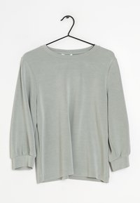 Lichtgrijs langemouwen shirt met ronde hals en omgeslagen mouwen, hangend aan een zwarte draadhanger tegen een witte achtergrond.