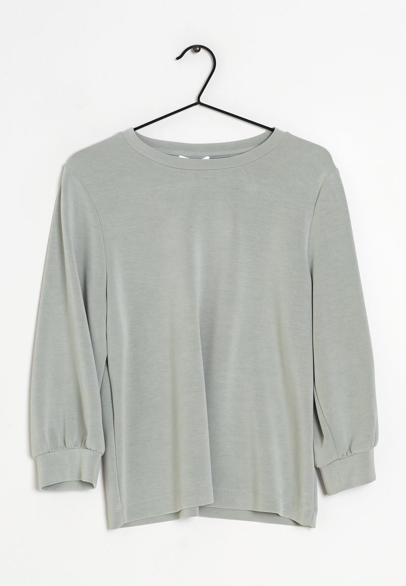 Lichtgrijs langemouwen shirt met ronde hals en omgeslagen mouwen, hangend aan een zwarte draadhanger tegen een witte achtergrond.