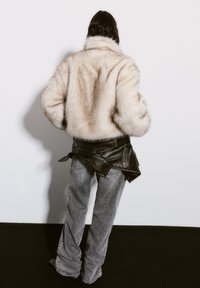 Faux fur beige jacket with a high collar, paired with gray flared jeans and a black leather utility belt, focusing on texture and layering.