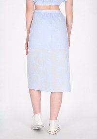 Lichtblauwe midi-rok met bloemenborduursels, elastische tailleband en een doorschijnende onderlaag. Gepaard met witte canvas sneakers.