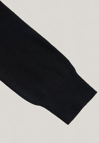 Czarna dzianinowa rękawica z teksturowanym wzorem, ściągaczem i gładkim wykończeniem. Materiał wydaje się miękki i elastyczny.