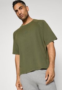 Olive zelené oversize tričko s krátkymi rukávmi, okrúhlym výstrihom a nenápadným logom. Ľahký bavlnený materiál, voľný strih.