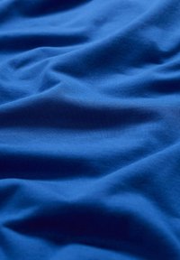 Kék pamutanyag enyhe textúrával és puha eséssel, sima, megszakítatlan felülettel és finom fényváltozásokkal.