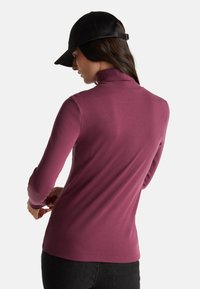 Maglia a maniche lunghe e collo alto di un profondo colore bacca, realizzata in un tessuto liscio ed elastico. Completa il look un cappellino nero con visiera curvata.