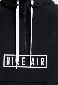 Nike Air černá pulovrová bunda s texturovaným povrchem. Má částečný zip, bílé stahovací šňůrky a výrazné bílé logo na přední straně.