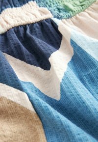 Gros plan d’un tissu doux et texturé avec des sections froncées et un motif géométrique dans des tons bleus, blancs, beiges et verts.