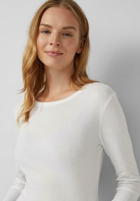 Witte langemouwtop met een ronde halslijn. Zacht, lichtgewicht materiaal met een gladde textuur. Eenvoudig ontwerp zonder patronen of accenten.