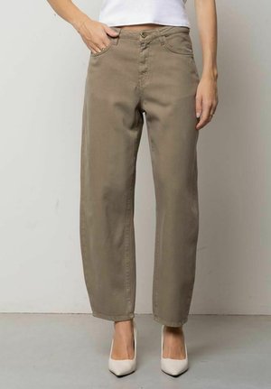 Donna che indossa pantaloni marroni a vita alta, gamba dritta con tasche frontali, abbinati a décolleté bianche con punta appuntita e top bianco corto.