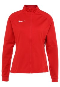 Rode Nike-jas met een hoge kraag, een volledige ritssluiting aan de voorkant en lange mouwen. Gemaakt van glad, lichtgewicht materiaal. Voorzien van een wit Nike-logo.