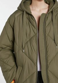 Olivgrön vadderad jacka med huva, som har en quiltad design, dragkedja framtill och dragsko detaljer. Mjukt, lättviktigt tyg.