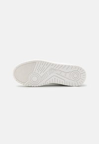 Weiße Sneaker-Sohle aus strukturiertem Gummi, mit kreisförmigen und linearen Mustern sowie einem Logo an der Ferse. Glatte Oberfläche mit rutschfesten Details.