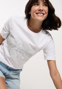 Biała bawełniana koszulka z krótkim rękawem z szarym, teksturowanym grafiką oraz napisem "Życie jest piękne" wraz z "Cross Jeans 1990".