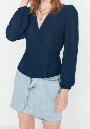 Marineblauw wikkelshirt van textuurstof met ballonmouwen, gecombineerd met een lichte denim minirok met een voorknit en rafelige zoom.