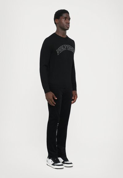 Black long-sleeve shirt with logo embroidery, paired with black pants and white sneakers. Smooth texture, fitted design, and minimalistic style.