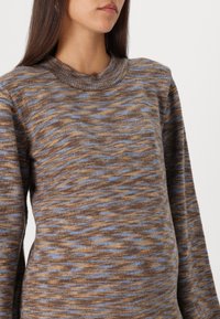 Pull en tricot texturé avec des motifs en vagues marron et bleu, col ras du cou et manches longues. Matière douce avec une coupe décontractée.
